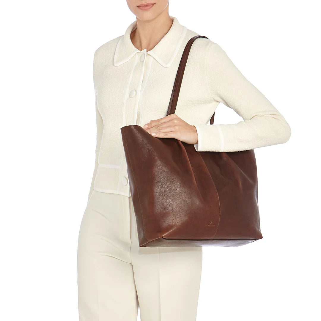 Model carrying the Il Bisonte Nina tote bag in coffee styled with elevated everyday and travel essentials